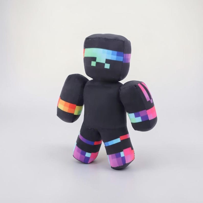 May include: A black plush toy figure with pixelated rainbow accents on the head, arms, and legs. The figure has a blocky design and a pixelated face. The arms and legs have rainbow-colored bands.