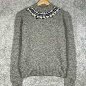 May include: A long-sleeved, heather gray knit sweater featuring a ribbed crew neckline, cuffs, and hem. The upper chest area displays a decorative circular yoke pattern in shades of dark blue, white, and light gray with intricate geometric details.