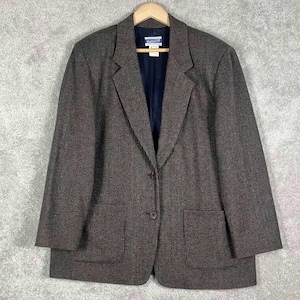 May include: A brown blazer with a subtle checkered pattern, featuring a single-button closure and two front pockets. The blazer has a navy blue lining and is hanging on a wooden hanger.
