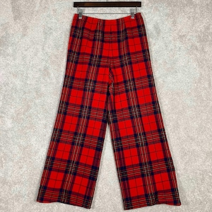 May include: Red plaid wide-leg pants hanging on a black hanger. The pants feature a bold red background with a classic plaid pattern in navy blue and yellow. The fabric appears to be a medium-weight material.