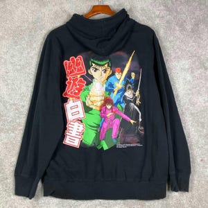 Peut inclure: Un sweat-shirt à capuche noir avec une grande impression graphique au dos. Le motif représente quatre personnages d'anime aux couleurs vives, notamment vert, bleu, rose et noir, accompagnés de caractères japonais en rouge et blanc.