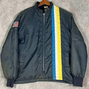 May include: A dark navy blue zip-up jacket featuring a stand-up collar and ribbed cuffs. The front displays a vertical stripe pattern in light blue, white, and yellow on the right side. A small American flag patch is sewn onto the right sleeve.