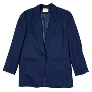 Puede incluir: Un blazer azul marino con cierre de un solo botón y dos bolsillos delanteros. El blazer tiene solapas con muescas y un corte entallado. El forro interior es de un tono azul más oscuro. Un estilo clásico.