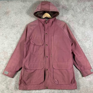 May include: A dusty rose hooded jacket featuring a front zipper closure with a snap-button placket, a chest pocket with a flap, two large lower pockets with flaps, and adjustable cuffs with hook-and-loop fasteners, lined with a plaid fabric.