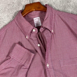 May include: A long-sleeve button-down shirt in a red and white micro-check pattern. The shirt features a button-down collar, a front placket with white buttons, and a chest pocket. The interior label reads Brooks Brothers Makers 16-3.
