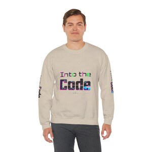 Pode incluir: Camisola bege com o texto "Into the Code" em uma fonte digital colorida no peito. As mangas têm texto adicional em um estilo semelhante. A camisola é de cor neutra.