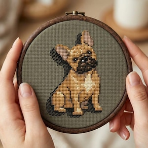 Può includere: Un ricamo a punto croce di un bulldog francese in un telaio di legno. Il cane è raffigurato in tonalità di marrone, beige e nero su uno sfondo verde tenue. Il telaio di legno è di colore marrone scuro.