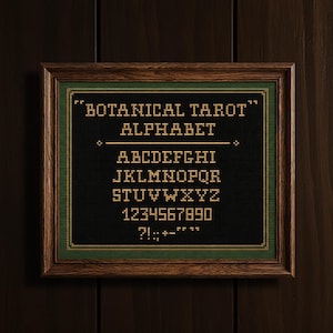 May include: A framed cross-stitch sampler with the text "BOTANICAL TAROT ALPHABET" and the alphabet, numbers, and punctuation. The sampler is black with gold and green stitching, set in a wooden frame.
