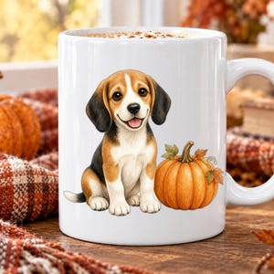 Peut inclure: Un mug en céramique blanche orné d'une illustration colorée d'un chiot beagle assis à côté d'une citrouille orange. Le chiot a un pelage marron, noir et blanc, et la citrouille est décorée de petites feuilles vertes et marron sur sa tige.