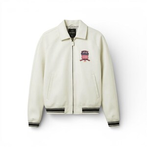 May include: Cream-colored jacket with a zip-up front, collar, and a patch on the chest. The patch features a shield design with red, white, and blue elements. The jacket has black and white striped cuffs and hem.