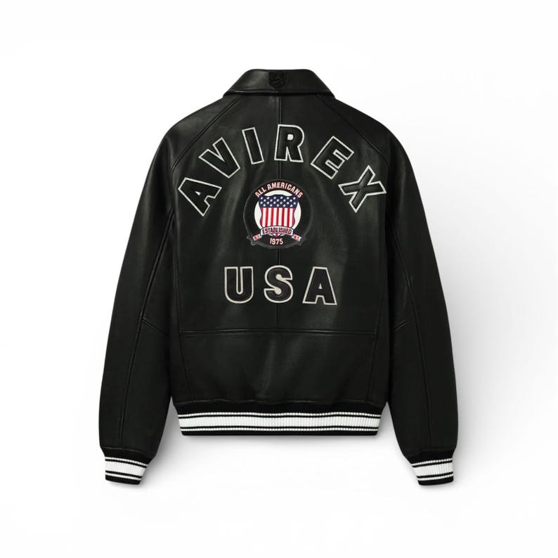 May include: Black leather jacket with white trim on the cuffs and hem. The back features the word "AVIREX" arched above a circular emblem with "ALL AMERICANS" and "1975" and the word "USA" below.