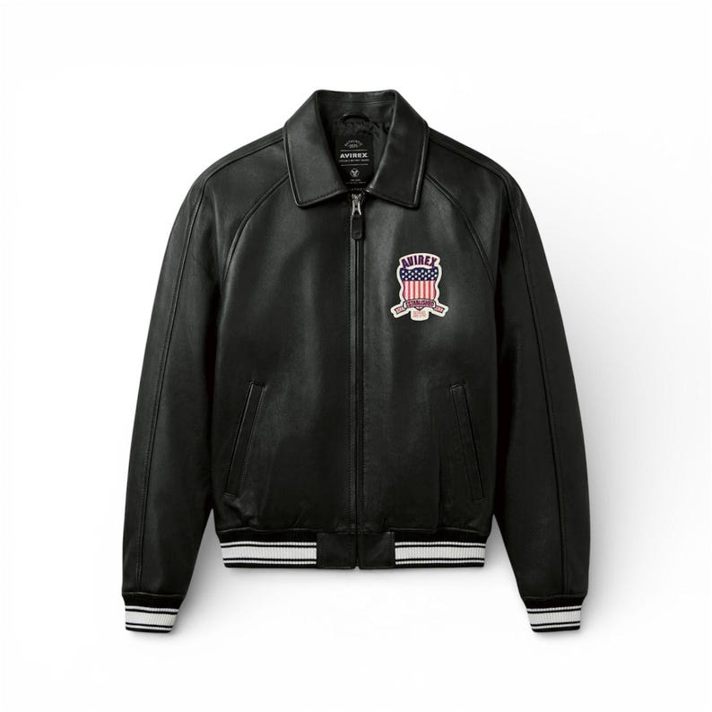 May include: Black leather jacket with a zip-up front, collar, and a patch on the chest. The patch features a red, white, and blue design with the word "AVIREX". The jacket has white and black striped cuffs and hem.