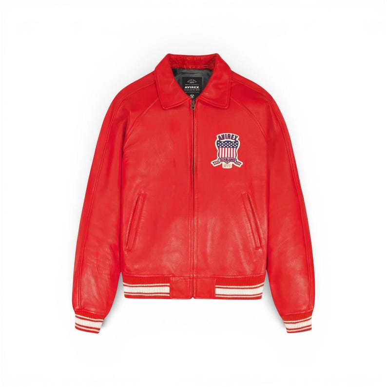 May include: A vibrant red leather jacket with a classic bomber style. Features a zip-up front, a collar, and a patch on the chest with the text "AVIREX" and a patriotic design. The cuffs and hem have white and red striped detailing.