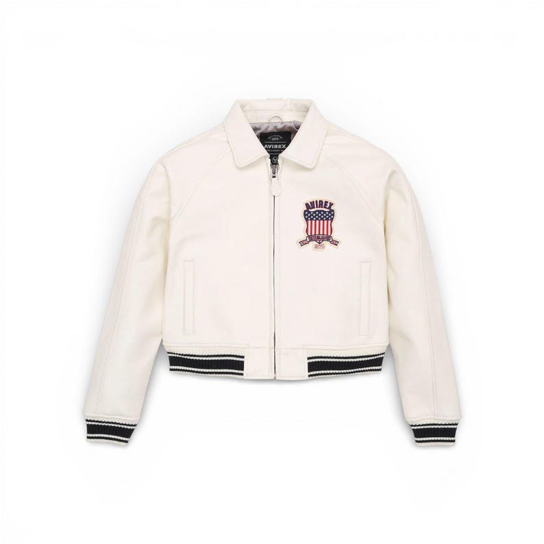Puede incluir: Chaqueta bomber color crema con cuello y cierre de cremallera. La chaqueta presenta un parche con un dise&ntilde;o de bandera americana y el nombre de la marca. Los pu&ntilde;os y el dobladillo tienen detalles a rayas blancas y negras.