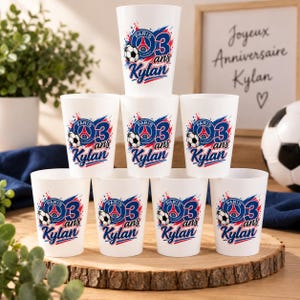 Könnte beinhalten: Ein Set aus acht weißen Kunststoffbechern in Pyramidenform, jeweils mit einer Grafik eines Fußballs, dem Paris Saint-Germain-Logo, der Zahl 3 sowie dem Schriftzug "ans" und "Kylan" in Blau und Rot für einen dritten Geburtstag.