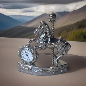 May include: A silver-toned carousel horse figurine featuring a round Elgin quartz clock integrated into the base. The horse is attached to a vertical pole with a spherical top, and the base is decorated with a repeating ribbon and rosette pattern.