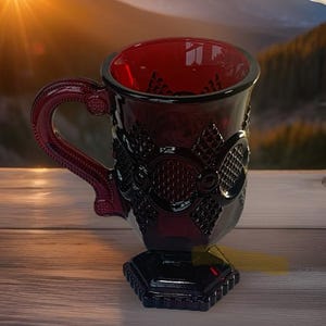 May include: A deep red glass mug featuring a textured diamond pattern on the exterior, a sturdy handle with decorative detailing, and a hexagonal base. The translucent ruby-colored glass catches the light, highlighting the intricate embossed design.