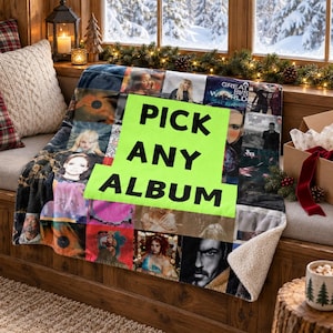 May include: A soft, plush throw blanket featuring a collage of various album cover images. A large, bright neon green rectangular patch is centered on the blanket with the black text "PICK ANY ALBUM" printed in bold, capital letters.