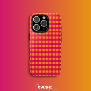Könnte beinhalten: Eine Handyhülle mit einem lebendigen rosa-orangenen Karomuster. Die Hülle hat eine glänzende Oberfläche und einen Kameraausschnitt mit mehreren Linsen. Der Markenname "THAT CASE STUDIO" ist unten aufgedruckt.