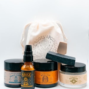 May include: A collection of skincare products including three jars and one amber glass pump bottle labeled Peace Roots Apothecary. The products are Peace Cream, Arise Herbal Eye Cream, Wild Yam Body Relaxant Cream, and Refresh. A black bar and wooden scoop sit in front of a beige drawstring bag.