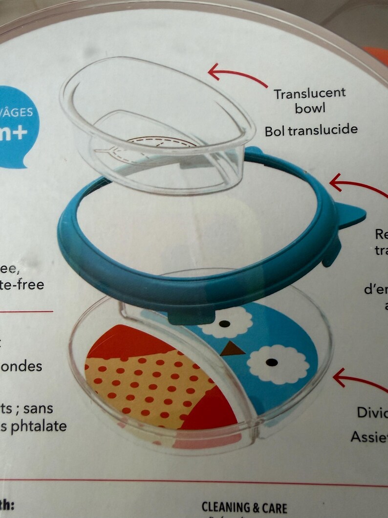 May include: A clear, divided baby bowl with a blue rim and a translucent lid. The bowl features a section with a red and tan polka-dot pattern and a section with a blue owl design. The text "Translucent bowl" is visible.
