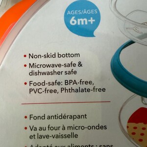 May include: A close-up of a baby food container package. The package features a blue speech bubble with "AGES/&Acirc;GES 6m+". The text on the package includes "Non-skid bottom" and "Microwave-safe & dishwasher safe".