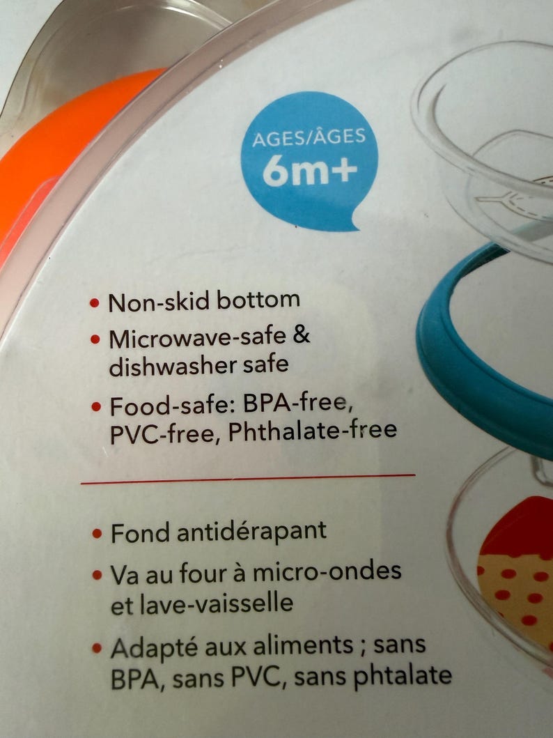 May include: A close-up of a baby food container package. The package features a blue speech bubble with "AGES/&Acirc;GES 6m+". The text on the package includes "Non-skid bottom" and "Microwave-safe & dishwasher safe".