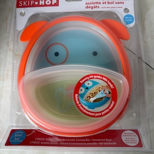 May include: A Skip Hop ZOO eat neat plate & bowl set in a clear plastic package. The set includes a divided plate, removable training rim, and translucent bowl. The bowl is blue with orange accents and a dog face design.