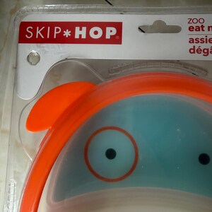 May include: A Skip Hop ZOO baby bowl with an orange rim and a blue interior. The bowl has a cartoon-like design with a large eye and a small orange fin. The packaging includes the Skip Hop logo in red.