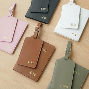 Può includere: Una collezione di etichette per bagagli e porta passaporti personalizzati in vari colori, tra cui rosa, marrone, grigio, bianco e nero. Ogni etichetta e porta passaporto presenta iniziali o nomi in lettere dorate, con chiusura a fibbia.