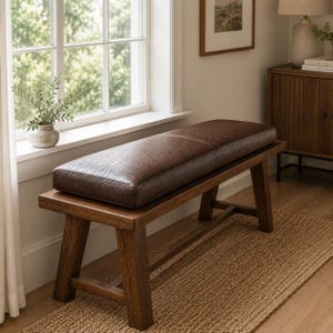 May include: A rectangular bench featuring a dark brown, textured leather-like upholstered seat cushion resting on a solid wooden frame with four angled legs and horizontal support stretchers connecting the legs on each side of the furniture piece.