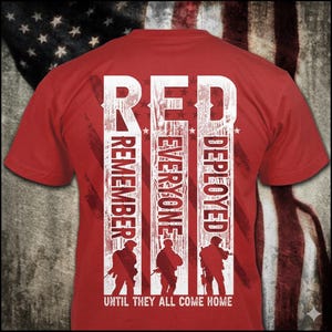 以下が含まれることがあります： 愛国的なデザインの赤いTシャツ。「RED REMEMBER EVERYONE DEPLOYED」の文字が白でプリントされ、兵士のシルエットが描かれています。「UNTIL THEY ALL COME HOME」のフレーズが下にあります。背景にはアメリカ国旗が描かれています。