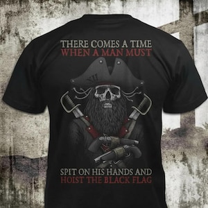 Puede incluir: Una camiseta negra de manga corta con el gráfico de una calavera con sombrero de pirata, barba, espadas cruzadas y dos pistolas de chispa. El texto dice: THERE COMES A TIME WHEN A MAN MUST SPIT ON HIS HANDS AND HOIST THE BLACK FLAG.
