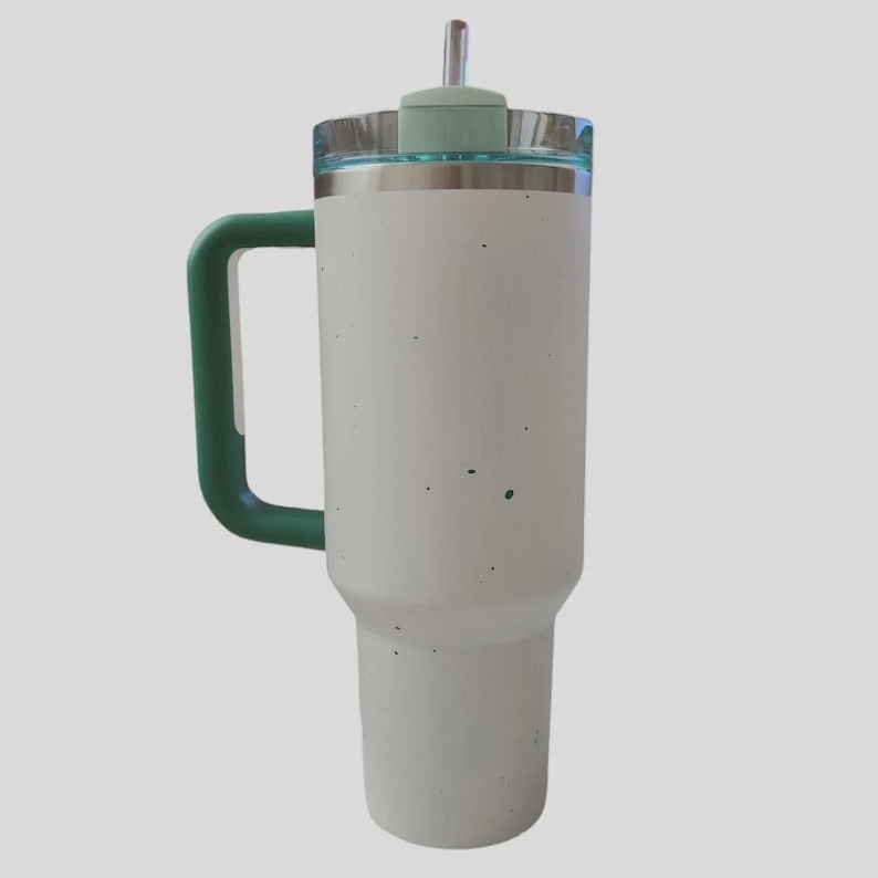 K&ouml;nnte beinhalten: Ein wei&szlig;er Isolierbecher mit gr&uuml;nem Griff und Deckel. Der Becher hat einen Edelstahlrand und einen transparenten Deckel mit gr&uuml;nem Oberteil und Strohhalm. Der Becher ist etwa 25 cm hoch.