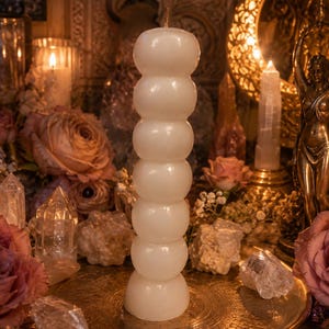 May include: A tall, off-white pillar candle with a stacked, spherical bubble design. The candle features a smooth, glossy surface and a single wick at the top, standing vertically as a singular, cylindrical object with a rounded, segmented shape.