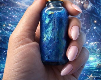 May include: A blue glass bottle with a gold cap and white dropper is held in a hand with pink nails. The bottle contains a shimmering, iridescent liquid. The background features a celestial and ocean-themed illustration with the text "Lulu's Magical Botanica".