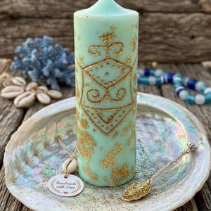 May include: A pale green pillar candle with gold glitter patterns and a white wick. The candle is on a pearlescent shell-shaped dish with a small spoon. A tag reads "Handmade with Love."