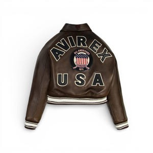 May include: Brown leather jacket with the text "AVIREX USA" on the back. The jacket features a patch with the words "ALL AMERICANS" and "ESTABLISHED 1975". The jacket has white and black striped cuffs and hem.