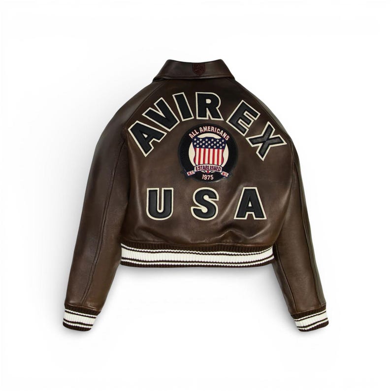 May include: Brown leather jacket with the text "AVIREX USA" on the back. The jacket features a patch with the words "ALL AMERICANS" and "ESTABLISHED 1975". The jacket has white and black striped cuffs and hem.