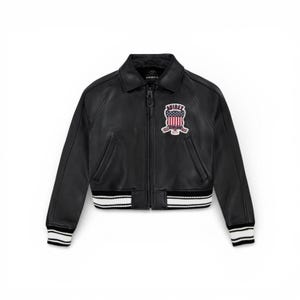 May include: Black leather jacket with a classic collar, zip closure, and a patch featuring a red, white, and blue emblem. The jacket has white and black striped cuffs and waistband. The brand name "AVIREX" is visible on the patch.