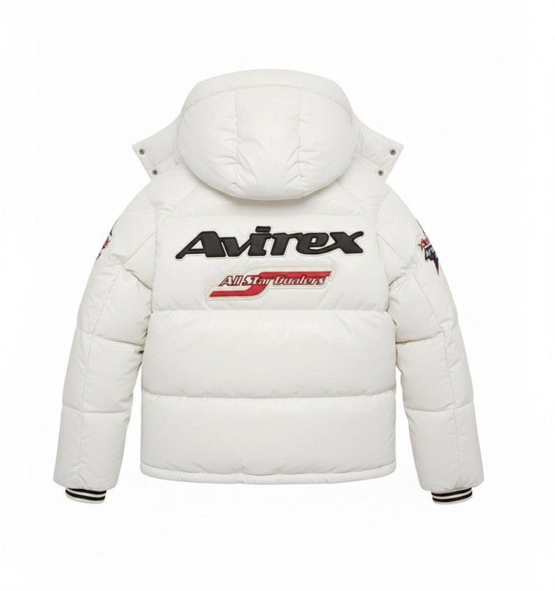 K&ouml;nnte beinhalten: Wei&szlig;e Pufferjacke mit Kapuze, mit dem Markennamen "Avirex" in schwarzer Schrift auf dem R&uuml;cken. Unter dem Markennamen steht der Text "All Star Hunters" in Rot und Wei&szlig;. Die Jacke hat schwarz-wei&szlig; gestreifte B&uuml;ndchen.