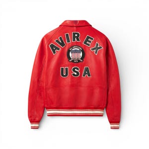K&ouml;nnte beinhalten: Eine leuchtend rote Lederjacke mit wei&szlig;en und schwarzen Akzenten. Auf dem R&uuml;cken steht in Wei&szlig; der Schriftzug "AVIREX" und "USA", mit einem Emblem der amerikanischen Flagge. Die Jacke hat einen klassischen Bomberstil mit gerippten B&uuml;ndchen und Saum.