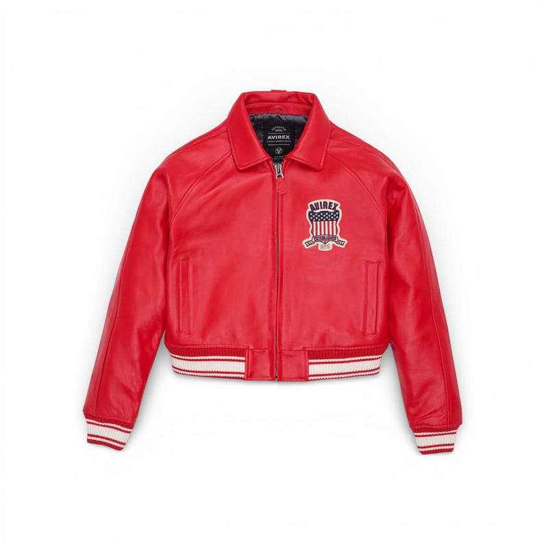 May include: A vibrant red leather jacket in a bomber style. It has a white and red striped ribbed hem and cuffs. The jacket has a zip-up front and a small chest patch with the text "AVIREX".