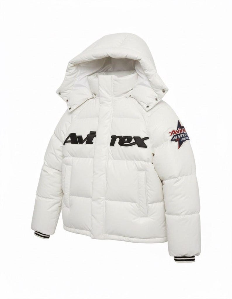 K&ouml;nnte beinhalten: Wei&szlig;e Pufferjacke mit Kapuze, mit dem Text "Avi rex" in Schwarz auf der Brust. Ein Aufn&auml;her mit Text und Stern-Design befindet sich am oberen linken &Auml;rmel. Die Jacke hat schwarz-wei&szlig; gestreifte B&uuml;ndchen.