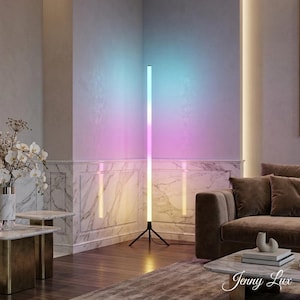 May include: A contemporary LED floor lamp with a black tripod base, emitting a gradient of colours. The lamp transitions through blue, pink, and yellow hues. The setting is a living room with a sofa, coffee table, and marble detailing.
