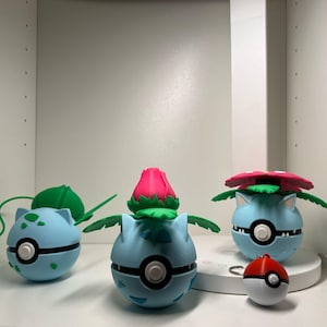 May include: A display of light blue, spherical figures with black and white details, reminiscent of a well-known character. Some have green leaves and pink or red flower-like tops. A red and white ball-shaped keyring is also included.