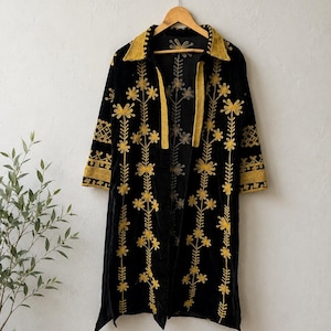 Könnte beinhalten: Ein schwarzer Langarm-Duster-Mantel mit leuchtend gelber Blumenstickerei auf der Vorderseite und an den Ärmeln. Das Kleidungsstück hat einen spitzen Kragen, ein offenes Vorderteil und einen geraden Saum, präsentiert auf einem Holzkleiderbügel.