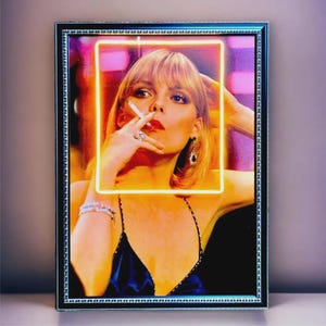 Può includere: Stampa artistica incorniciata con una donna bionda che fuma una sigaretta. Indossa un vestito blu scuro e gioielli. L'immagine è incorniciata con una cornice nera e un quadrato giallo neon intorno al viso della donna.
