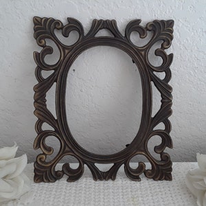 May include: An ornate, oval-shaped picture frame with a dark brown finish and intricate scrollwork details.