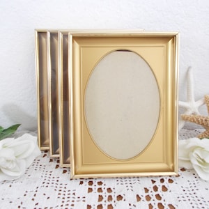 May include: Set of three gold-colored picture frames with oval openings. The frames are stacked on top of each other.